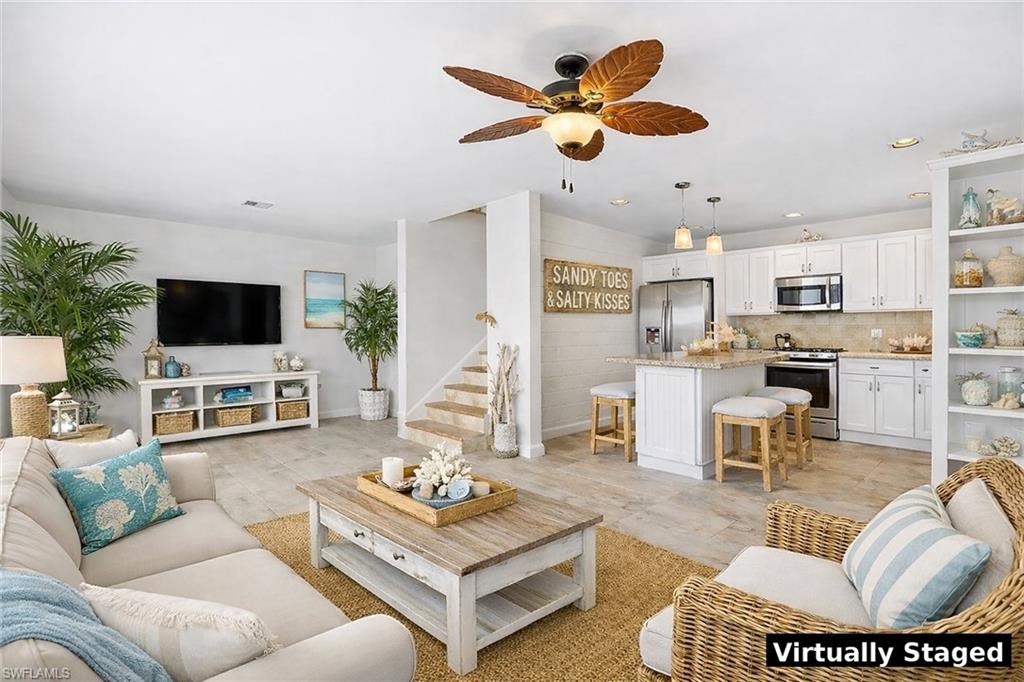 Open-concept living space featuring wood-finish flooring, a contemporary kitchen with white cabinetry, stainless steel appliances, and a central island with bar seating