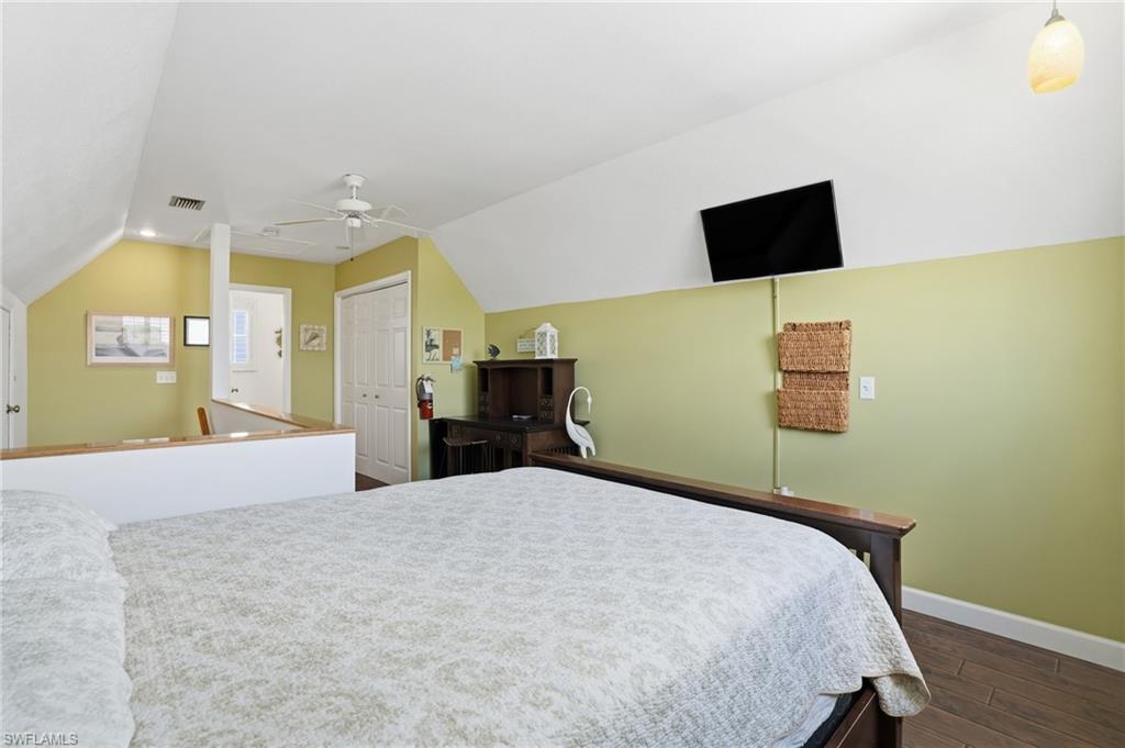 Bedroom featuring wood-finish flooring, a wall-mounted television, a built-in ceiling fan, and bi-fold closet doors