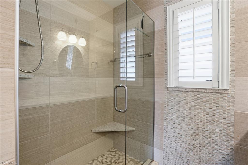 Glass-enclosed shower featuring a tiled surround, built-in corner shelf, and pebble-style flooring