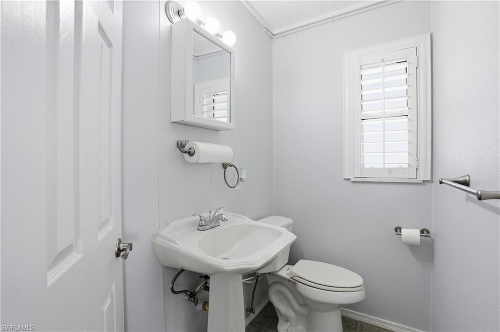 Pedestal sink with chrome faucet, wall-mounted medicine cabinet with integrated lighting, window with white plantation shutters, and light blue wall paneling