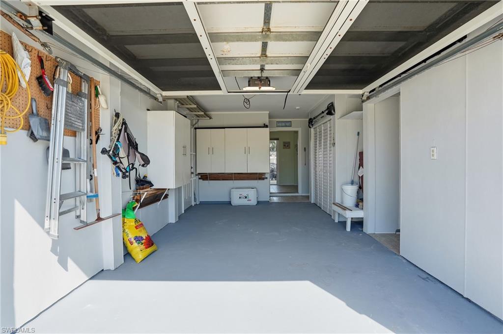 Spacious garage featuring a durable gray floor, built-in storage cabinetry, white wall panels, and a functional pegboard organization system
