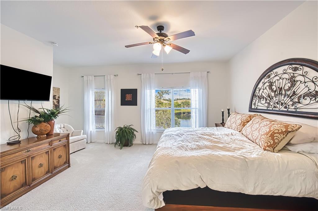 Spacious bedroom featuring light-colored carpet flooring, two windows with blinds and sheer curtains, and a ceiling fan with integrated lighting