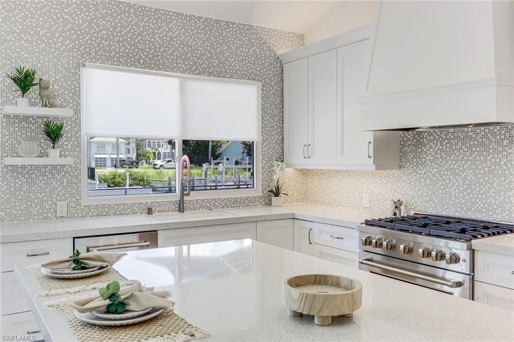 Spacious kitchen featuring white shaker cabinetry, an integrated range hood, a stainless steel gas range, and light-toned mosaic tile backsplash