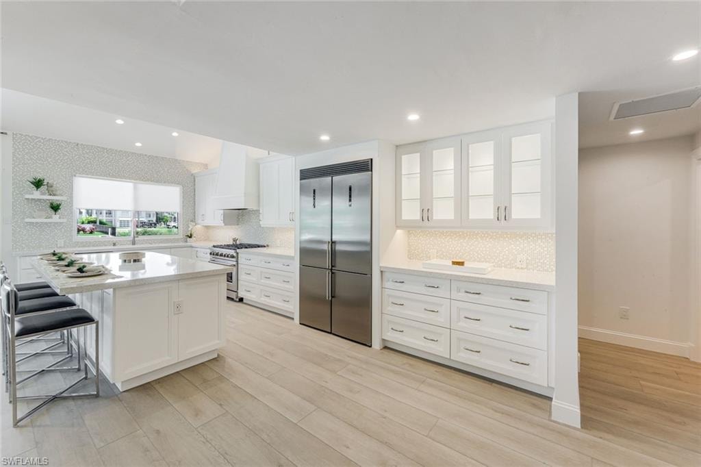 Bright kitchen featuring white cabinetry, a large center island with seating, stainless steel appliances, and wood-finish flooring