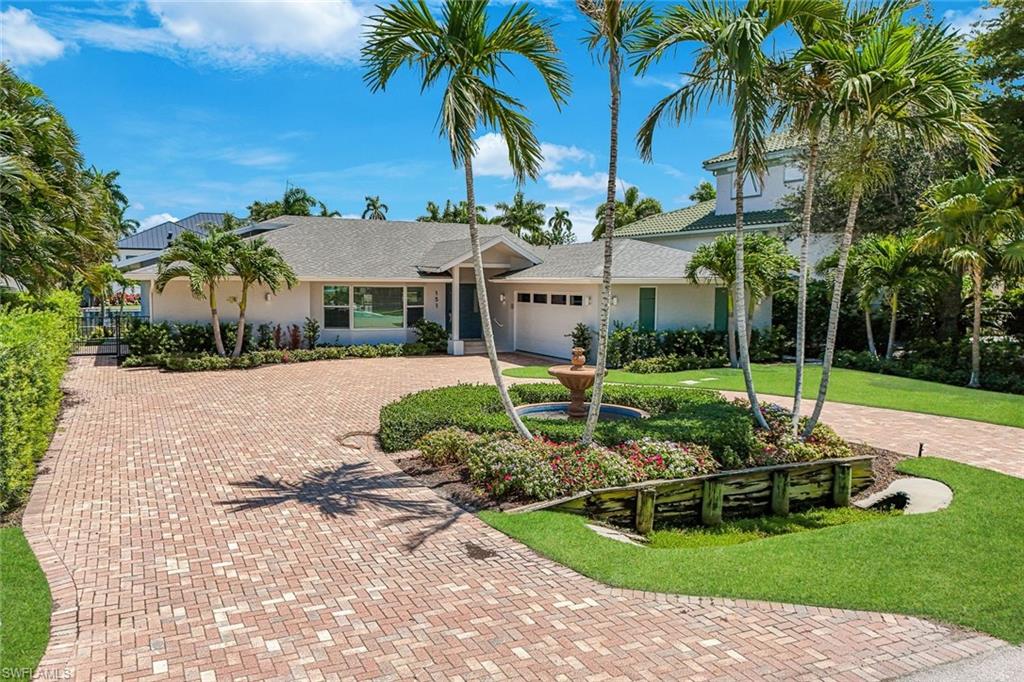Expansive brick paver driveway with circular element, flanked by manicured lawns and lush tropical landscaping