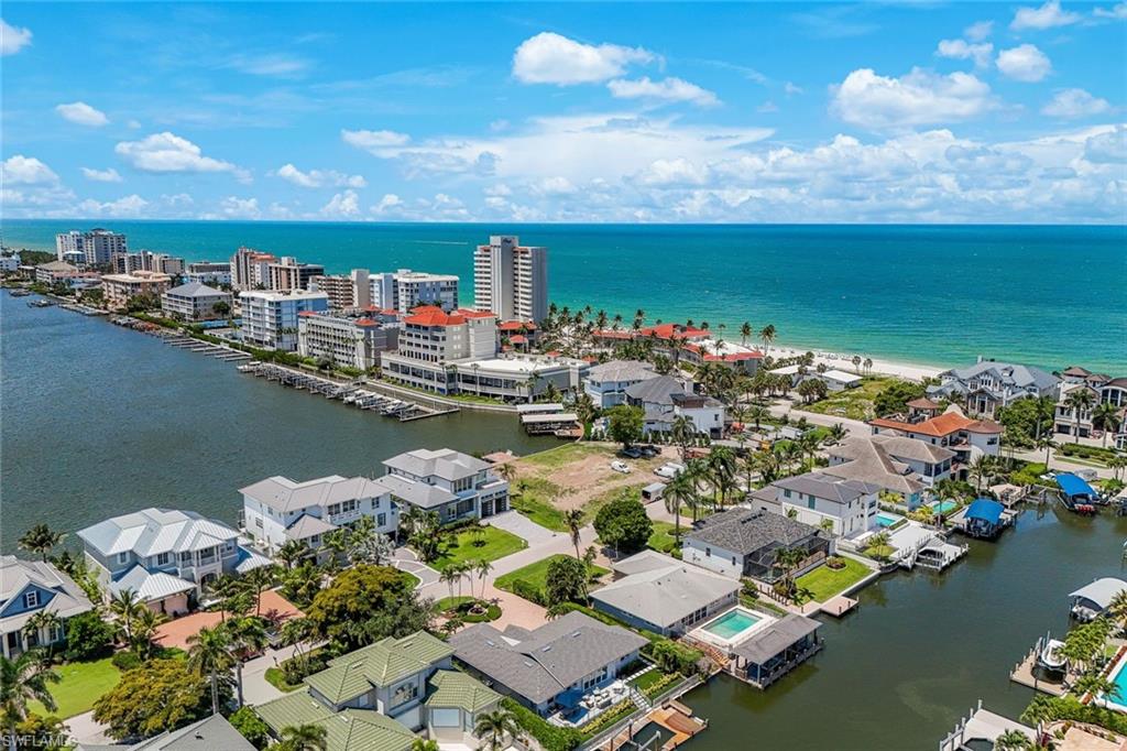 Coastal residential area featuring waterfront properties, numerous docks, direct access to open water, a sandy beach, and a distant city skyline