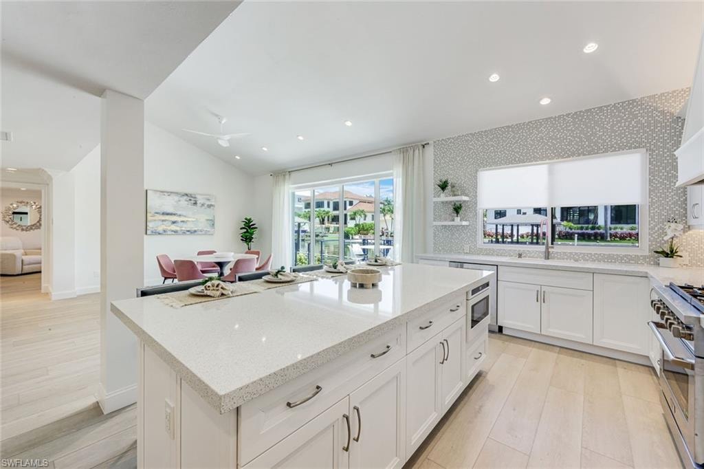 Spacious kitchen featuring a large island with a light-colored countertop, white cabinetry with dark pulls, wood-finish flooring, recessed lighting, and a window with a water feature backdrop