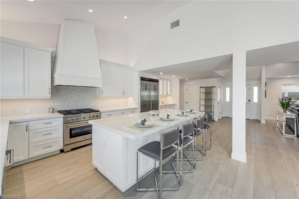 Open-concept kitchen featuring white shaker cabinetry, an integrated range hood, stainless steel appliances, a center island with seating, and wood-finish flooring