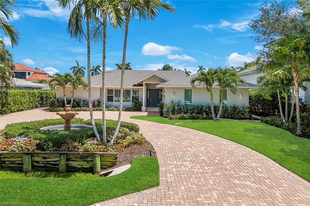 Contemporary stucco exterior with a brick paver driveway, a central water feature, and mature palm trees