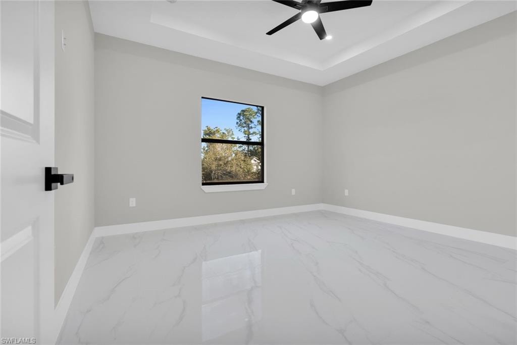 Spacious room featuring large format tile flooring, crown molding, a tray ceiling, and a ceiling fan with integrated lighting