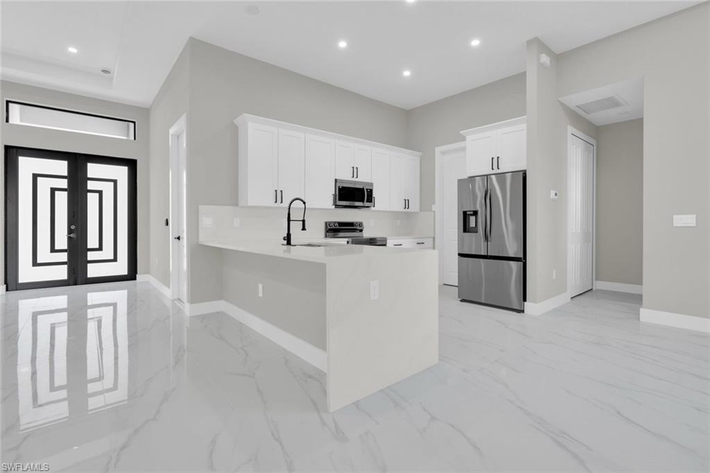 Kitchen featuring white cabinetry, stainless steel appliances, a white island with an undermount sink, and recessed lighting
