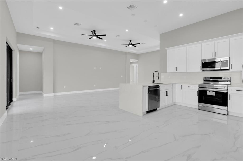 Open-concept kitchen featuring white cabinetry, stainless steel appliances, a center island with a sink, and light-toned flooring