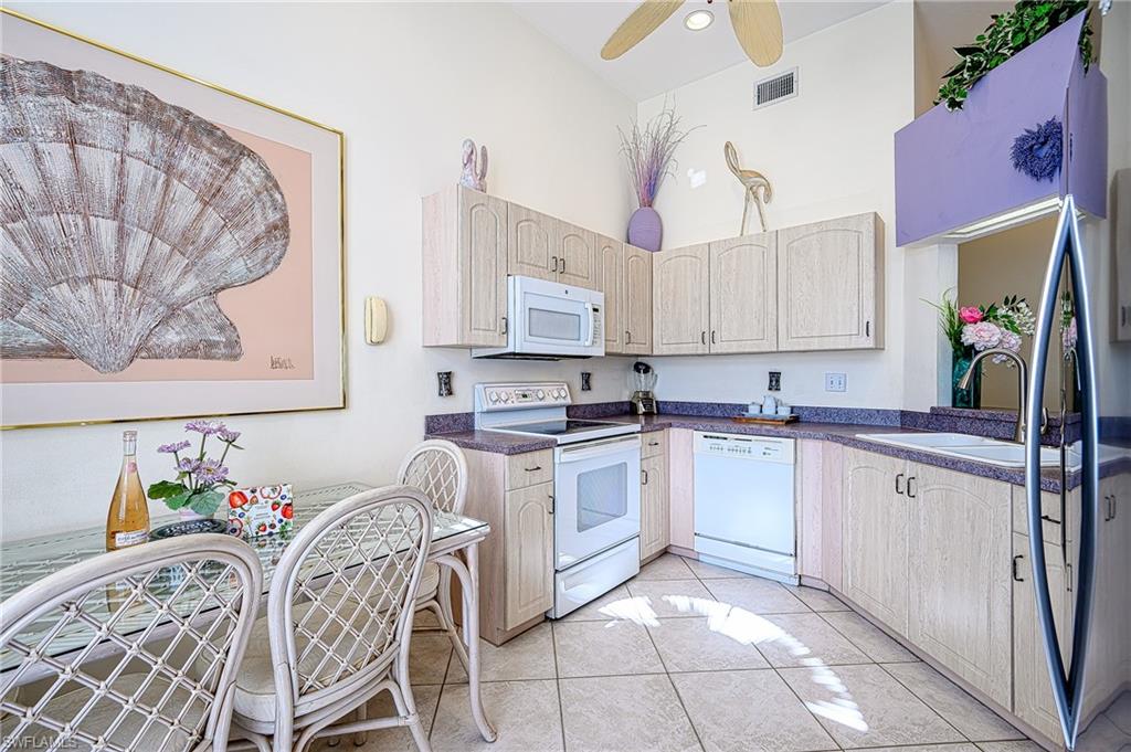Kitchen with white appliances, dark countertops, a ceiling fan, light tile patterned floors, and light brown cabinetry