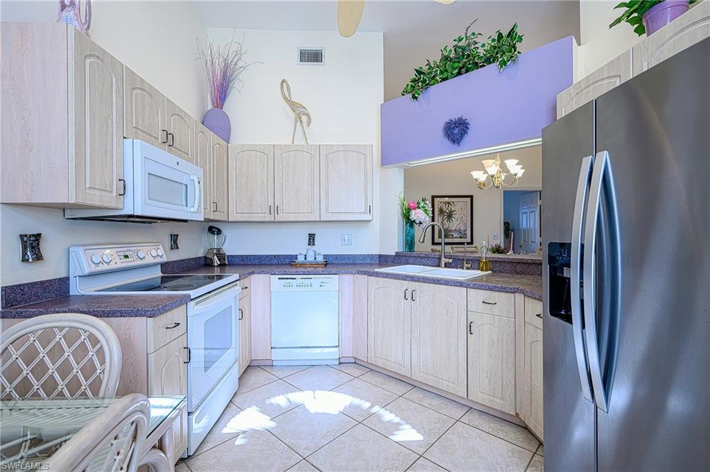 Kitchen featuring white appliances, dark countertops, a chandelier, and light tile patterned floors