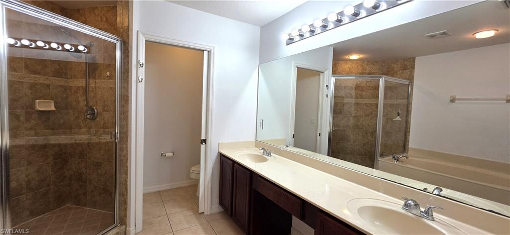 Bathroom featuring a glass-enclosed shower with tile surround, a dual vanity with undermount sinks and light-toned countertop, and a built-in tub