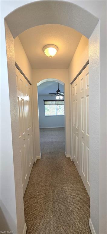 Arched entryway leading to a carpeted hallway with bifold closet doors