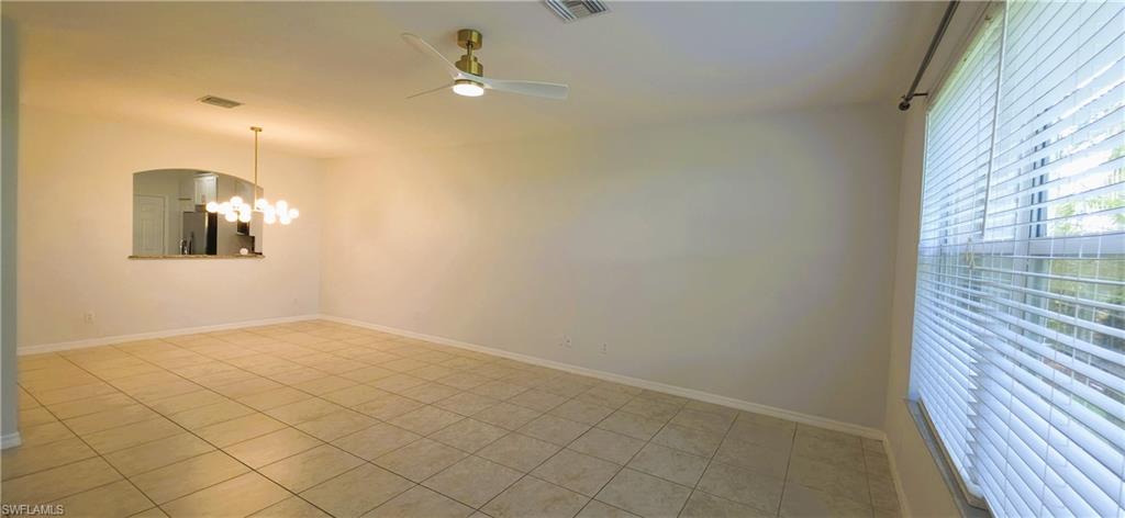 Spacious room featuring neutral tile flooring, a contemporary ceiling fan, and a pass-through window with an arched opening