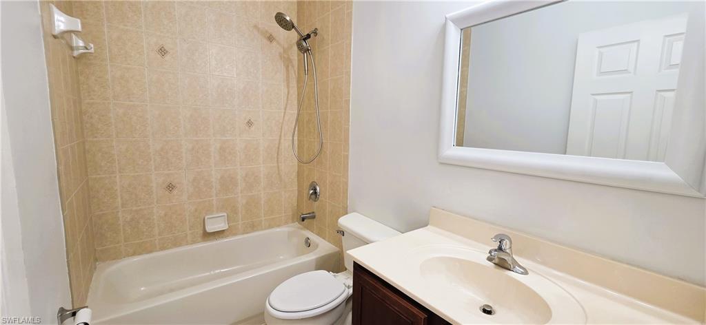Bathroom featuring a bathtub with shower, tiled surround with accent tiles, toilet, and vanity with an integrated sink and framed mirror
