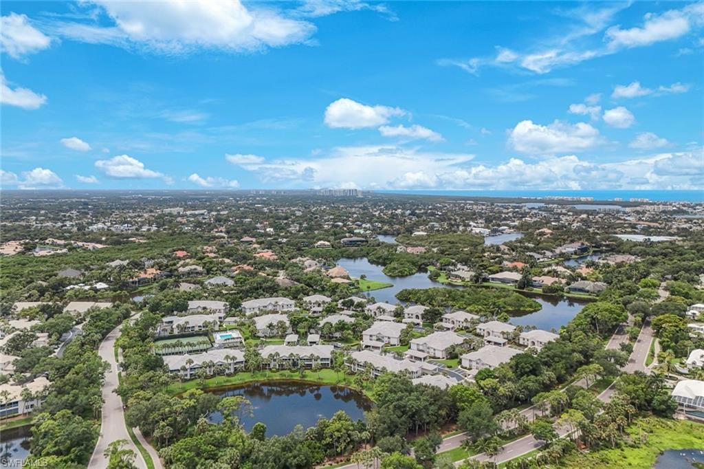 Expansive aerial perspective showcasing a residential community with abundant green spaces, multiple water features, and distant coastal elements