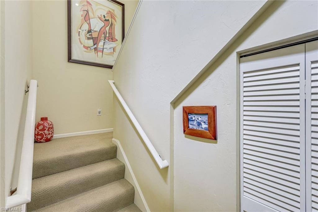 Carpeted staircase featuring white handrails and bi-fold louvered doors