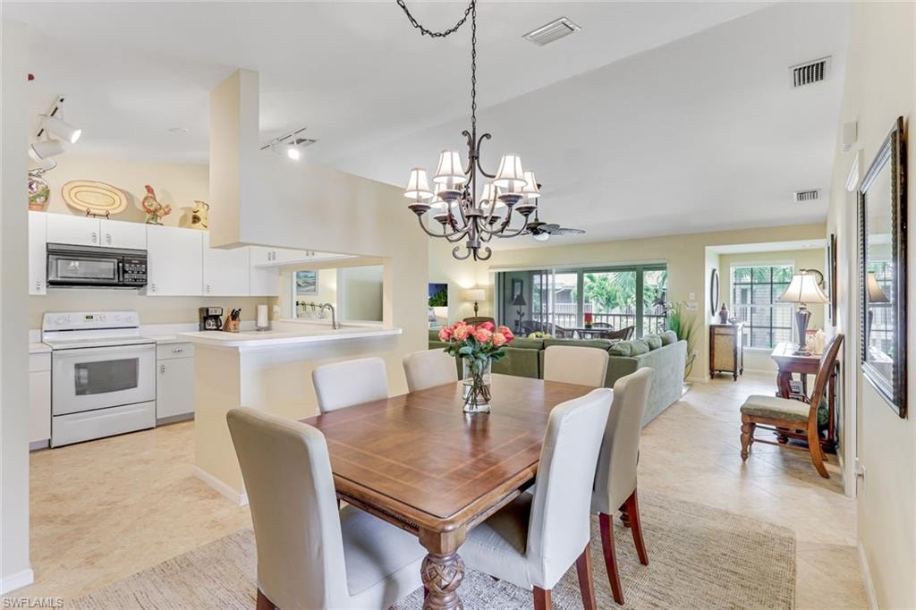 Open-concept living space featuring a dining area with a chandelier, a kitchen with white cabinetry and appliances, and a living room with exterior access
