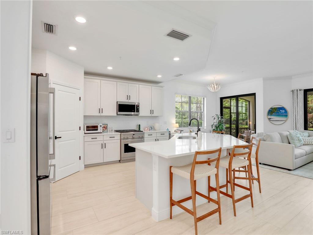 Kitchen featuring appliances with stainless steel finishes, a sink, open floor plan, light countertops, and white cabinetry