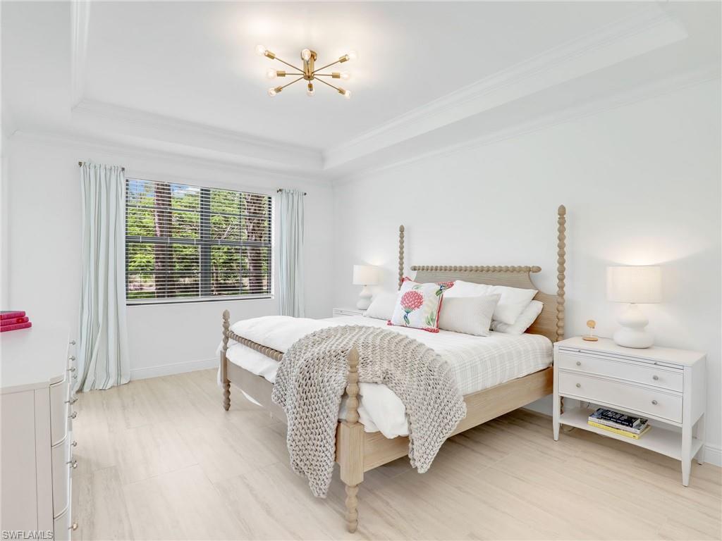 Bedroom featuring a tray ceiling, crown molding, a chandelier, and baseboards