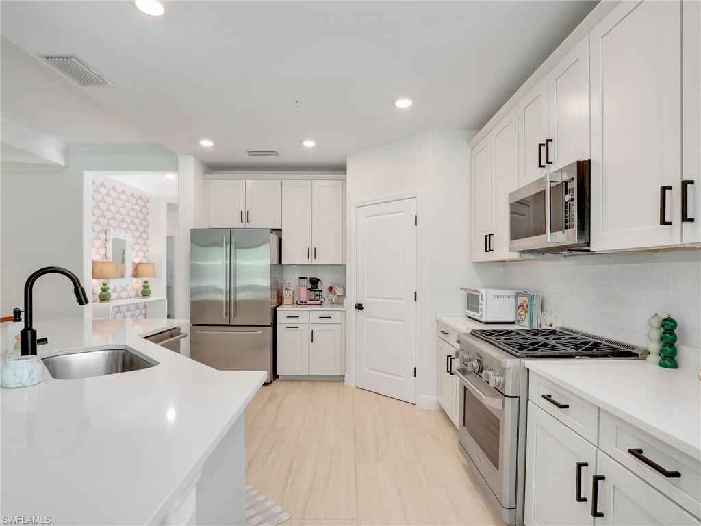 Kitchen with appliances with stainless steel finishes, a sink, light countertops, white cabinetry, and backsplash