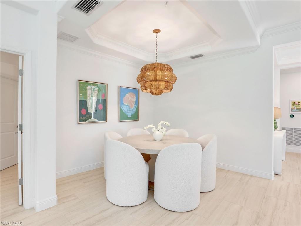 Dining room with a chandelier, baseboards, a raised ceiling, and crown molding