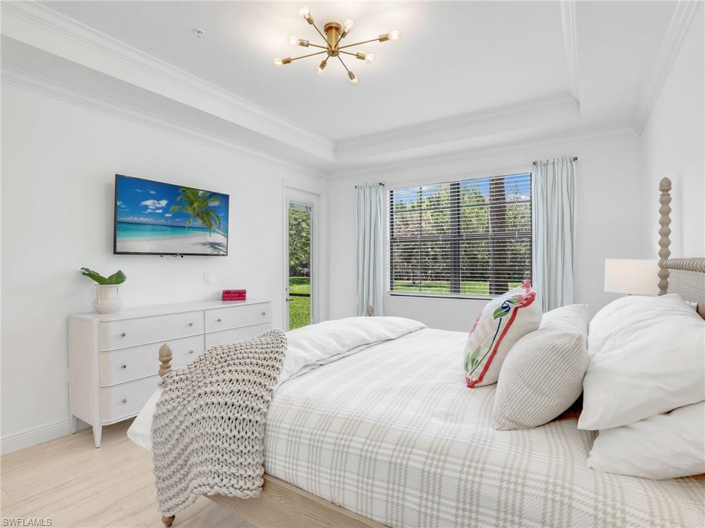 Bedroom with a raised ceiling, light wood-style floors, a chandelier, crown molding, and baseboards