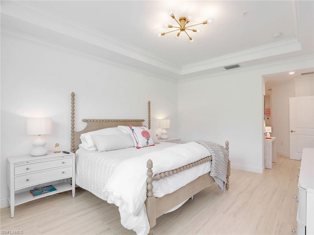 Bedroom featuring light wood finished floors, crown molding, a raised ceiling, baseboards, and a chandelier
