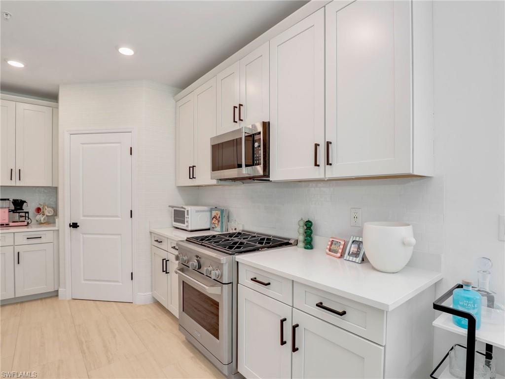 Kitchen with stainless steel appliances, decorative backsplash, light countertops, white cabinetry, and recessed lighting