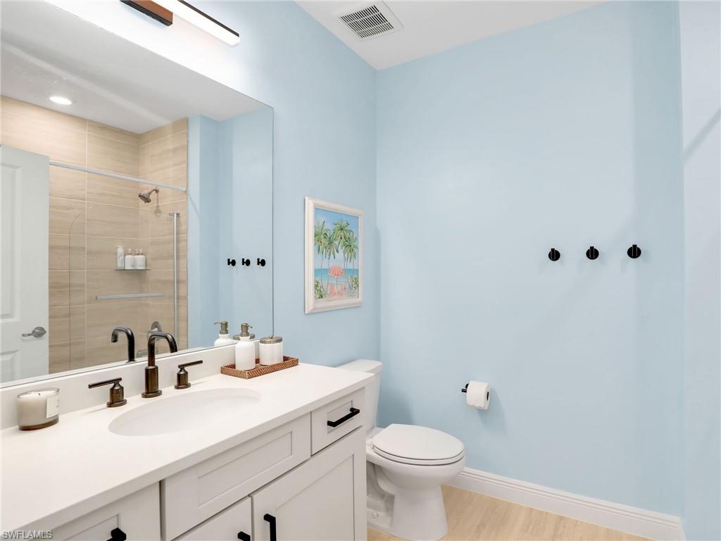 Bathroom featuring vanity, toilet, tiled shower, wood finished floors, and baseboards