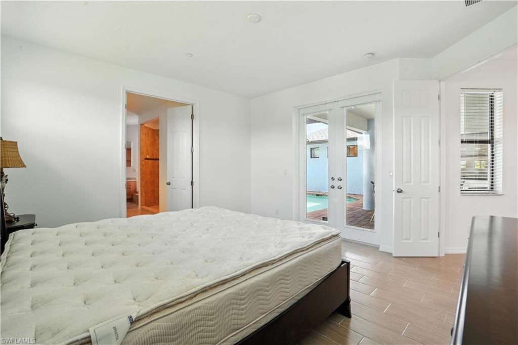 White wall interior featuring light-toned wood-finish flooring, French doors opening to an outdoor area with a pool, an additional interior doorway, and a window with horizontal blinds