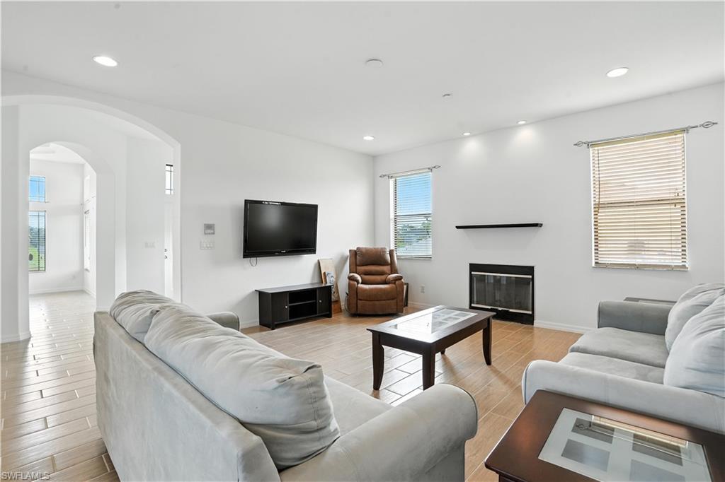 Living area featuring wood-finish flooring, a fireplace with a black mantel, recessed lighting, and an arched entryway