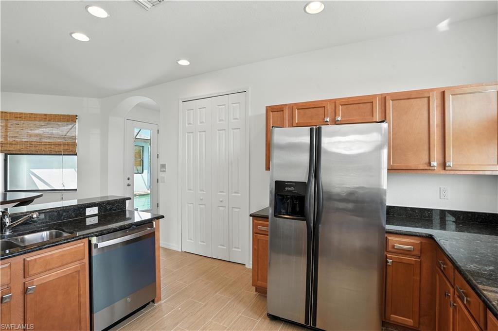 Kitchen featuring wood cabinetry, stainless steel appliances, dark stone countertops, and recessed lighting