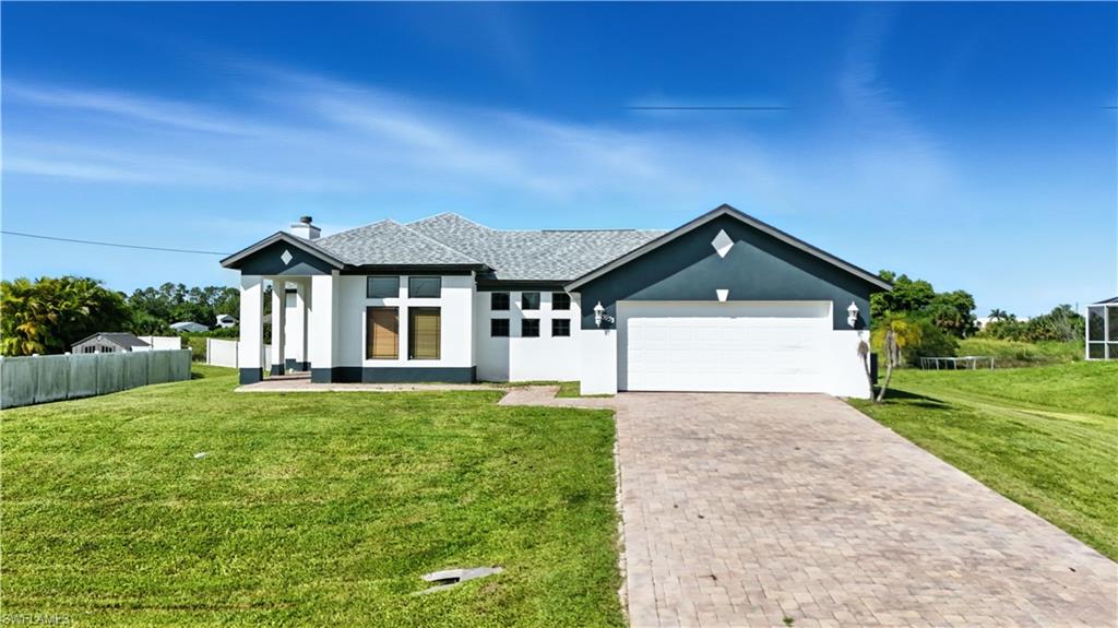 Contemporary single-story residence featuring a two-car garage, paver driveway, and a well-maintained lawn