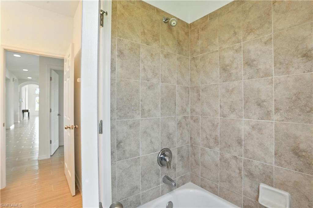 Bathtub with tiled shower surround, chrome fixtures, and a ceiling-mounted shower head