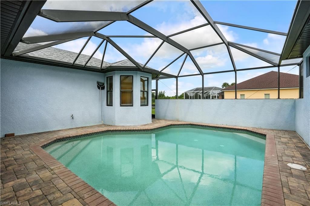 Screen-enclosed swimming pool featuring a paver deck surround and a bay window architectural detail