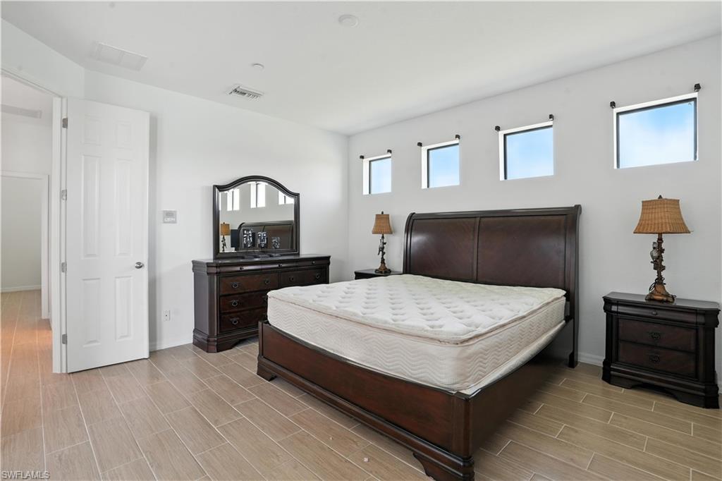 Spacious bedroom featuring light wood-finish tile flooring, crisp white walls, and four high-set windows