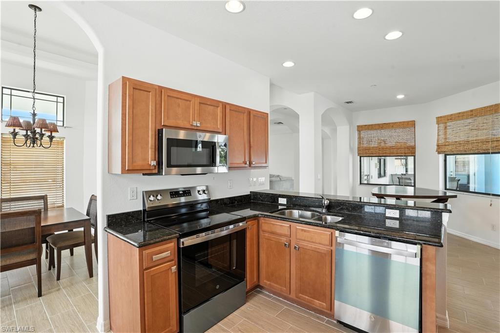 Kitchen featuring stainless steel appliances, wood cabinetry, dark stone countertops, and tile flooring