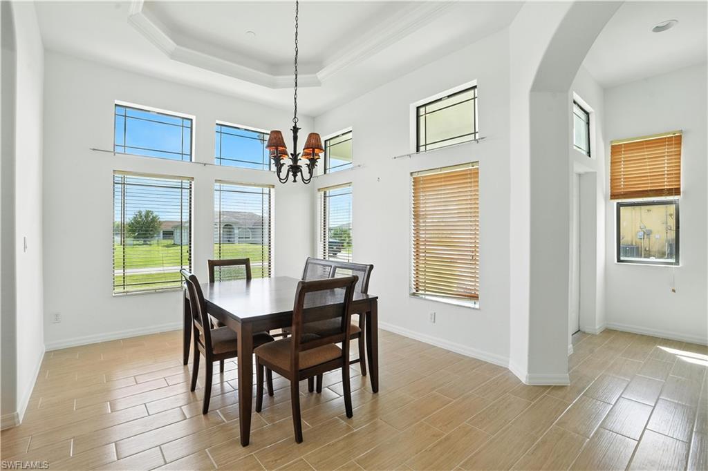 Tray ceiling with crown molding, natural light from multiple windows, ceramic tile flooring, and arched entryway