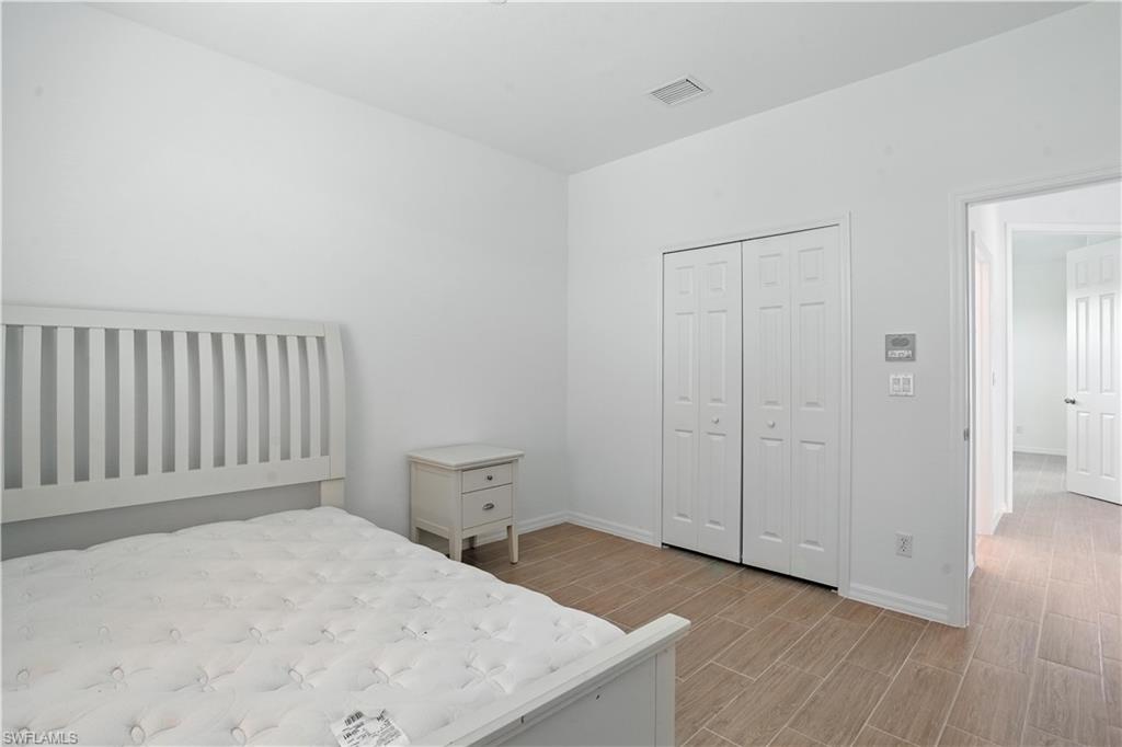 Spacious room featuring wood-finish flooring, white walls, and a ceiling-mounted air vent