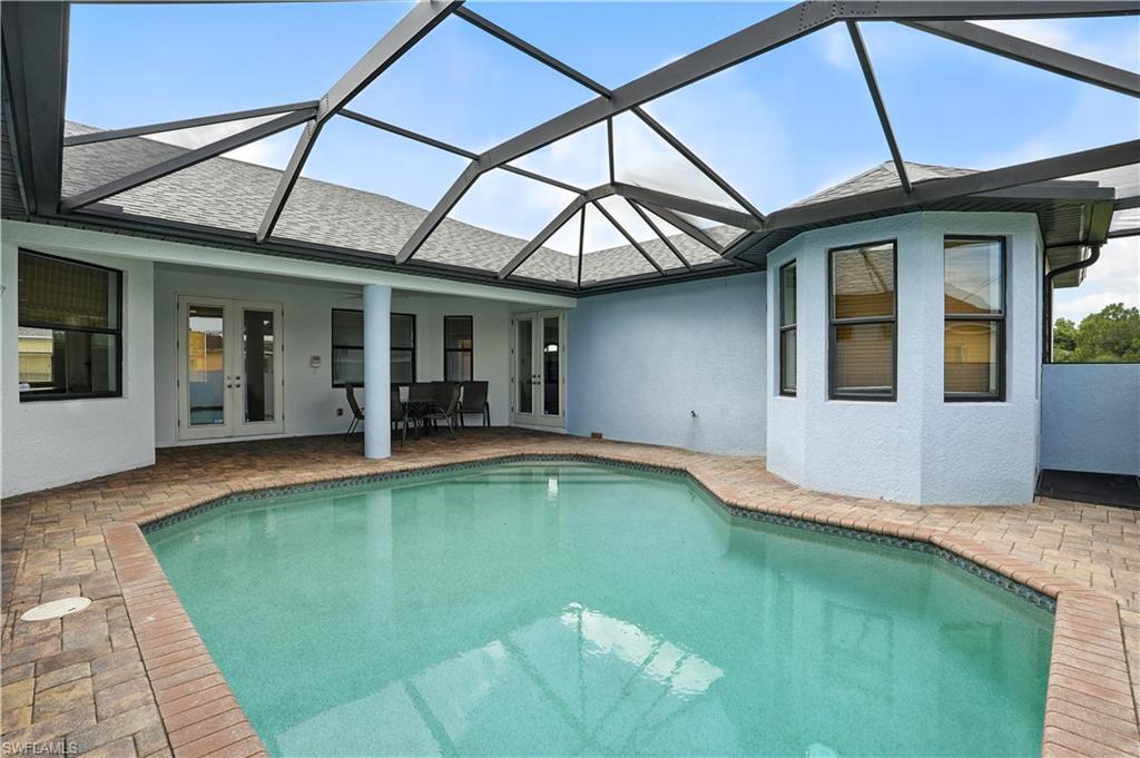 Screen-enclosed pool area featuring a freeform pool with brick paver decking, a light blue exterior wall, and multiple windows and French doors accessing the main structure