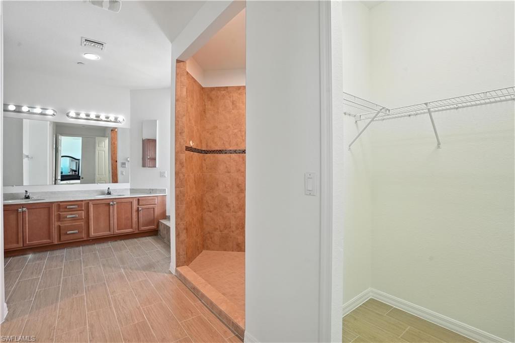 Bathroom featuring a walk-in shower with tile surround, dual vanity with undermount sinks, wood-finish cabinetry, and wood-look flooring