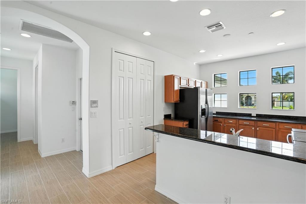 Bright kitchen featuring recessed lighting, a black appliance suite, wood cabinetry, dark countertops, and multiple windows