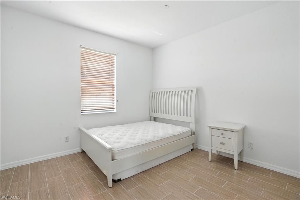 Bedroom featuring wood-finish tile flooring, white baseboards, a window with horizontal blinds, and clean white walls