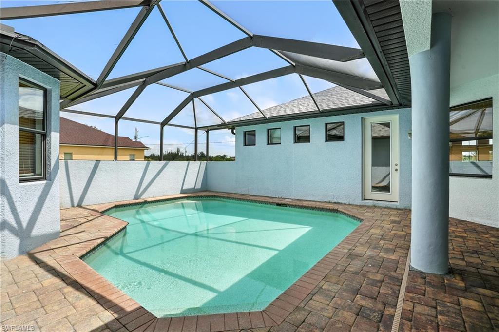 Screened-in swimming pool featuring a cool-toned finish, geometric shape, and surrounding brick paver decking