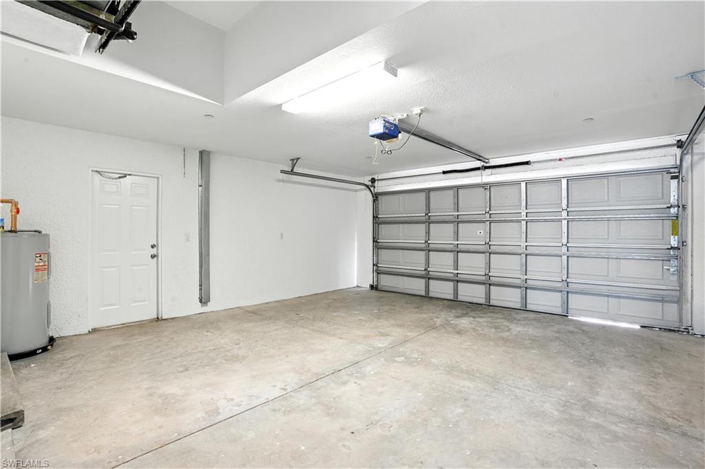 Spacious garage featuring a concrete floor, overhead lighting, a white interior door, a water heater, and an automatic garage door opener