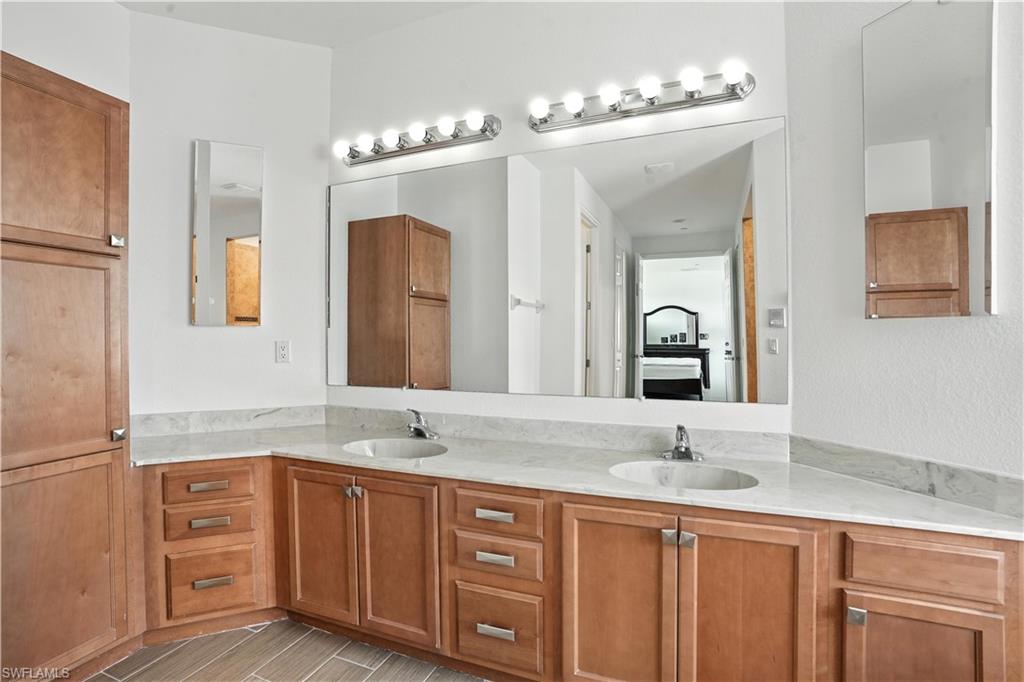Dual vanity featuring light-toned wood cabinetry, stone countertops, and integrated sinks
